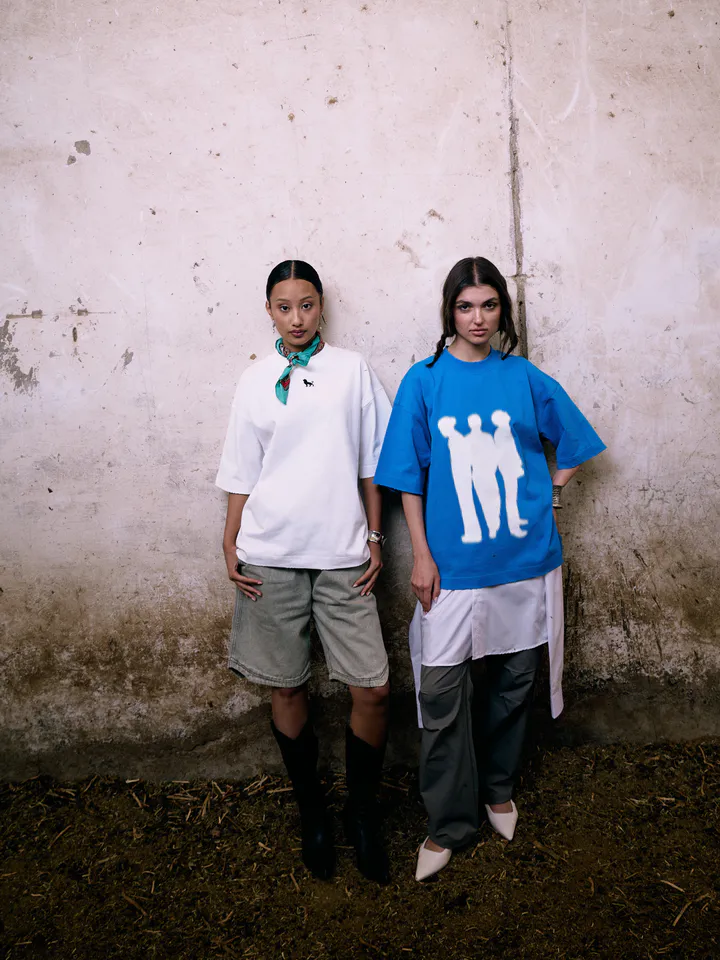 Two women in oversized Lion SA t-shirts standing against a weathered white wall