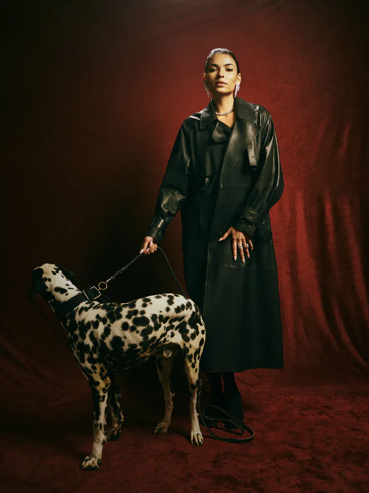 Woman in a black leather coat seated beside a Dalmatian against a deep red backdrop, Michael Oro Jewellery editorial