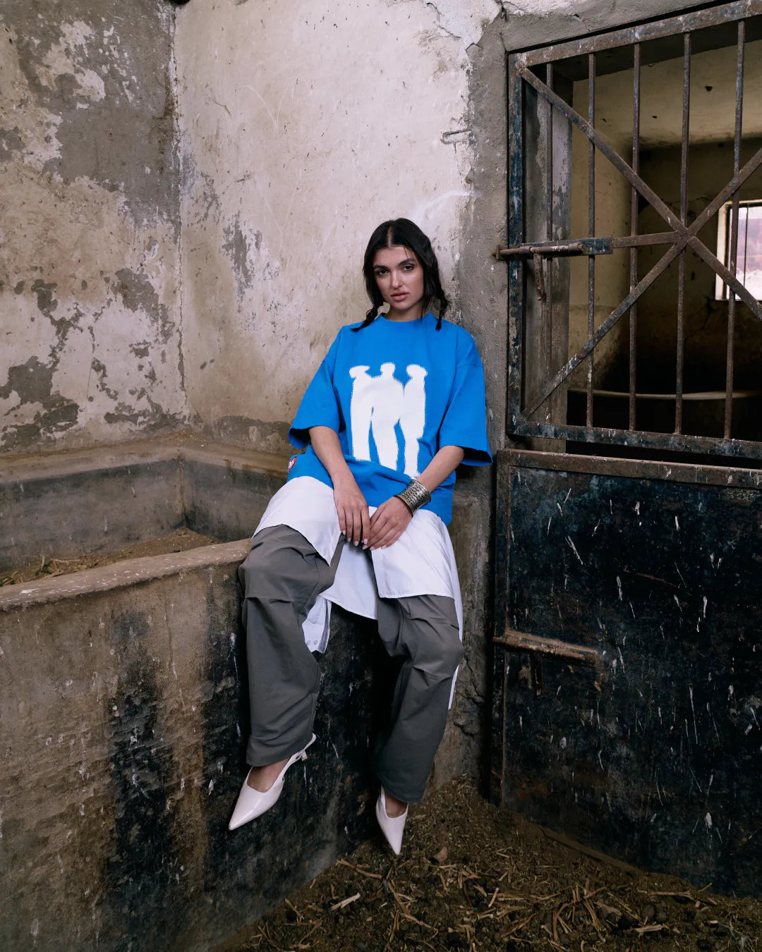 Woman in a bright blue Lion SA t-shirt sitting on a stone ledge in a rustic stable